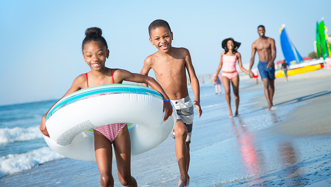 A family of four walks on the beach with a large inflatable raft.