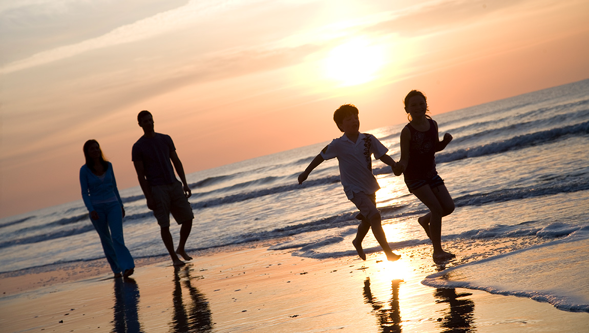 A family of four enjoys a sunset stroll along the beach.