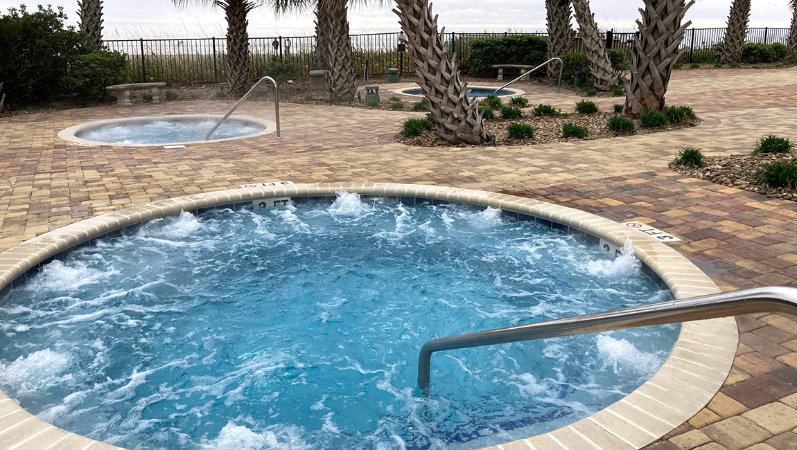 A hot tub with bubbles and a handrail, surrounded by palm trees and paver stones.