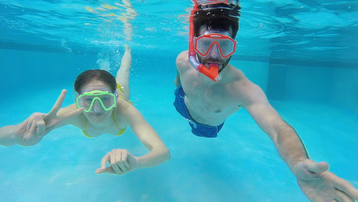 Two people swimming underwater in a pool.